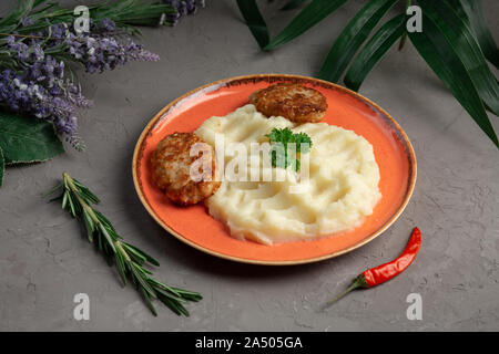 Purè di patate e costolette di carne in una piastra di colore arancione su sfondo grigio Foto Stock