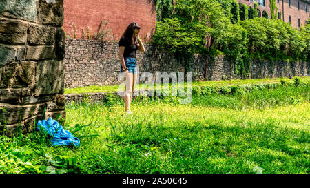 Teen girl in piedi in erba con pantaloncini blu e nero camicetta guardando in giù accanto a Chesapeake e Ohio Canal Foto Stock
