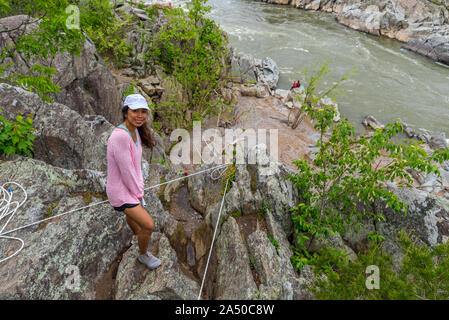 Donna in maglia rosa in piedi dal bordo della scogliera con funi di arrampicata e il fiume in background Foto Stock