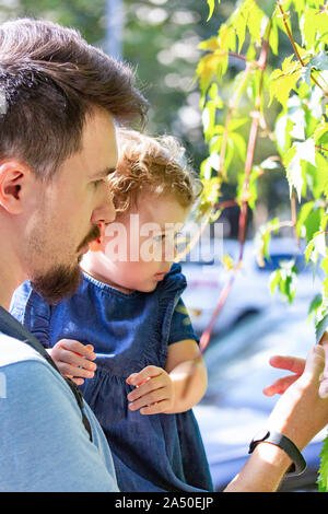 Un giovane padre e figlia guardare il liana. Caucasian brunette con un baffi e barba in profilo contiene una bambina. Ritratto verticale, parenth Foto Stock