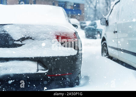 Macchina parcheggiata su una strada di città ricoperta di neve spesso strato durante la tempesta di neve la bufera di neve in inverno. Coda del veicolo a freddo inverno mattina nevicata. La sicurezza Foto Stock