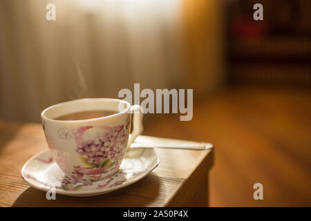 Il tè nero in un elegante vintage tazza di porcellana con il vapore sul tavolo Foto Stock