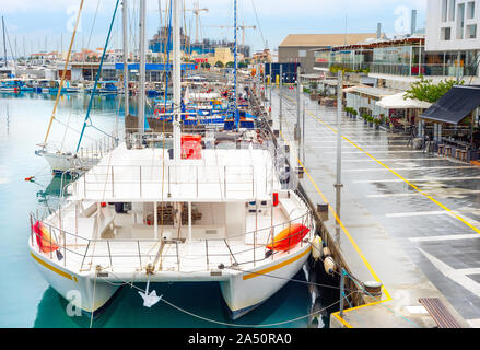 Catamarano, yacht e barche a motore ormeggiata nel porto di Limassol con caffè e ristoranti, giornata piovosa, Cipro Foto Stock