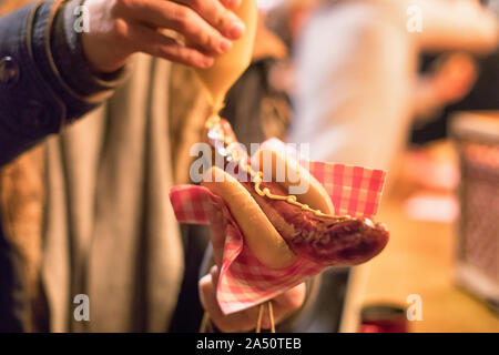 applicare la senape su una salsiccia in un panino Foto Stock