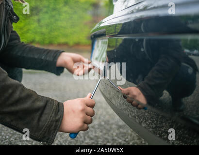 Una persona che ruba la targa su una macchina con un cacciavite Foto Stock