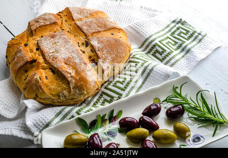 Un filone di oliva presi direttamente dal forno con un piatto di olive nere e verdi. Foto Stock