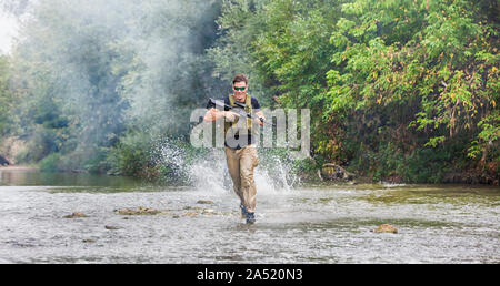 Piena esperienza militare - un giorno commando - in esecuzione attraverso l'acqua con un fucile Kalashnikov AK-47 replica Foto Stock
