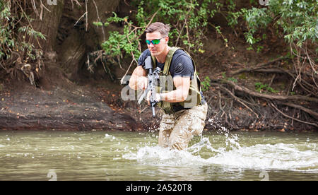 Piena esperienza militare - un giorno commando - in esecuzione attraverso l'acqua con un fucile Kalashnikov AK-47 replica Foto Stock