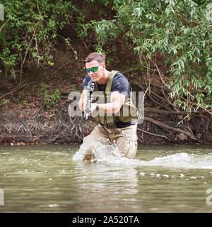 Piena esperienza militare - un giorno commando - in esecuzione attraverso l'acqua con un fucile Kalashnikov AK-47 replica Foto Stock