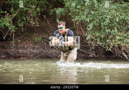 Piena esperienza militare - un giorno commando - in esecuzione attraverso l'acqua con un fucile Kalashnikov AK-47 replica Foto Stock