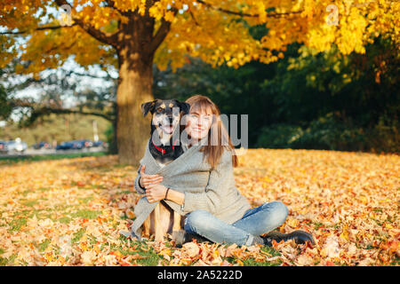 Ritratto di bella felice caucasico giovane donna seduta su un terreno tra autunno cadono le foglie giallo e abbracciando il suo cane. Migliori amici divertendosi o Foto Stock