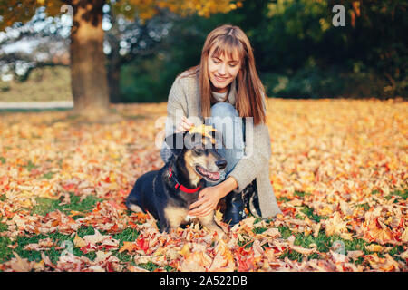 Ritratto di bella felice caucasico giovane donna seduta su un terreno tra autunno cadono le foglie giallo e abbracciando il suo cane. Migliori amici divertendosi o Foto Stock