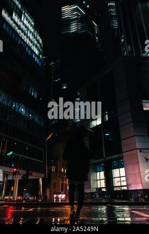Donna in piedi sotto la pioggia di fronte ad alto ufficio business edifici e grattacieli Foto Stock