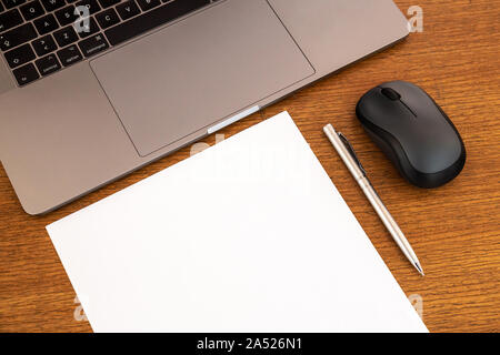 Desktop di lavoro in legno minimale con pagina vuota, spazio di copia, penna, laptop, mouse. Vista dall'alto, spazio di testo, immagine. Scrivania da ufficio. Foto Stock