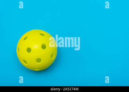 Di colore giallo brillante pickleball o sfera whiffle su un solido aqua blue piatto sfondo laici che simboleggiano sport e attività con copia spazio. Foto Stock