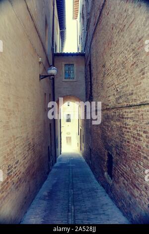 Foto verticale di molto bella strada stretta nella famosa città di Urbino. La città si trova sulla lista UNESCO. Gli edifici sono su entrambi i lati con passaggio di giunzione tra Foto Stock