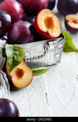 Prugne fresche con foglie in un metallo boxon un tavolo di legno vicino fino Foto Stock