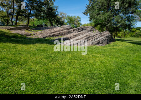 Luce diurna parco all'aperto prato con grande roccia stratificata e alberi Foto Stock