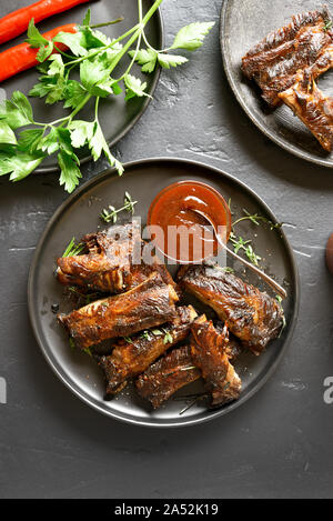 Piccante grigliate di costine sulla piastra su pietra nera dello sfondo. Gustosi barbecue di carne. Vista superiore, laici piatta Foto Stock