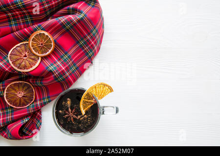 Natale rimuginassero vino rosso con secchi Arance su una tavola di legno tavolo bianco. Tradizionale bevanda calda in inverno. Modello di tartan scozzese di tessuto. Copia dello spazio. Foto Stock