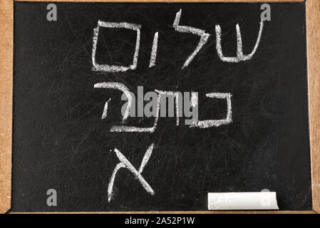 Si torna a scuola. Lavagna a fogli mobili o lavagna con Ciao di prima classe di qualità dei messaggi di saluto in lingua ebraica shalom Kita Alef scritta in gesso bianco sulla lavagna nera. Foto Stock