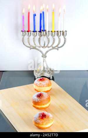 Immagine della festa ebraica Hanukkah sfondo con menorah candelabri tradizionale chiamato anche Hanukiyah, gelatina o marmellata ciambella sufganiyot e candele accese. Foto Stock