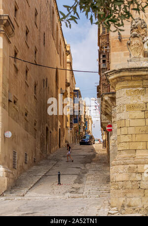 Ragazza giovane incrocio tipica strada di La Valletta con la strada in salita con scale e tradizionale maltese balconi in legno nella distanza. Foto Stock