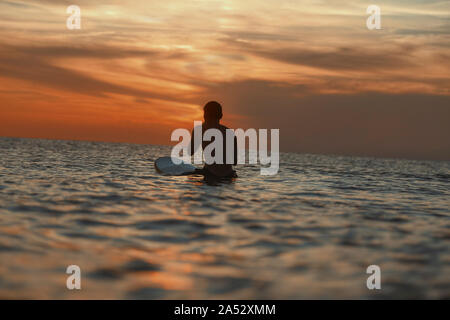 Surfer nell'oceano al tramonto Foto Stock