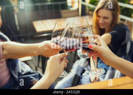 Persone tintinnanti bicchieri di vino sulla terrazza del bar o ristorante. Felice allegro amici celebrare in estate o in autunno fest. Immagine ravvicinata di mani umane, lo stile di vita. Foto Stock