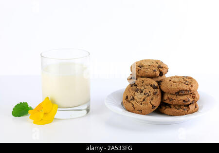 Piastra con i biscotti al cioccolato e un bicchiere di latte su sfondo bianco Foto Stock