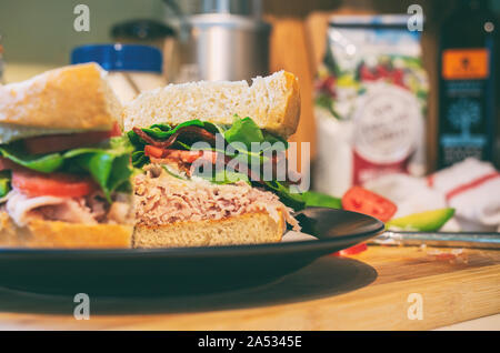 Turchia club sandwich tagliato a metà fatta con pancetta, pomodoro, avocado e lattuga su fresco cotto al forno del pane di pasta acida. Foto Stock