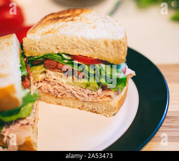 Turchia club sandwich tagliato a metà fatta con pancetta, pomodoro, avocado e lattuga su fresco cotto al forno del pane di pasta acida. Foto Stock