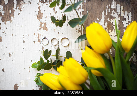 Gli anelli di nozze con tulipani gialli sul vecchio tavolo bianco Foto Stock