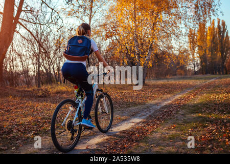 Giro in bicicletta allenamento nel parco d'autunno. Giovane donna biker con zaino in sella a una moto di caduta nella foresta. Una sana formazione all'aperto Foto Stock