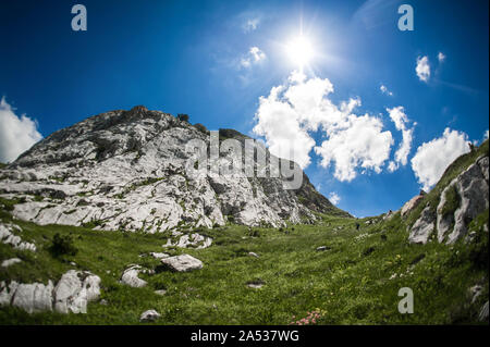 Estate montagna paesaggio. Prato con enormi pietre tra l'erba sulla sommità della collina vicino al picco della gamma della montagna Foto Stock