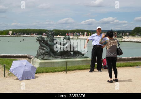 Versailles, Ile de France / Francia - Giugno 21, 2016: turisti cinesi in posa e scattare foto di fronte alla statua di bronzo del Re Nettuno in una Versa Foto Stock