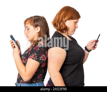 Orizzontale di studio shot di una madre e figlia appoggiata di schiena ogni utilizzando il proprio telefono cellulare. Sfondo bianco. Foto Stock