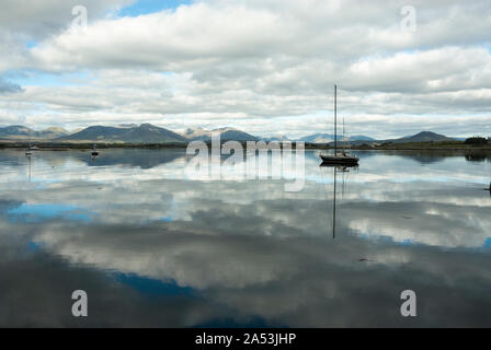 Riflessi di nuvole in acque ancora di Roundstone Haven, con barche e montagne distanti. Wild Atlantic modo. Foto Stock