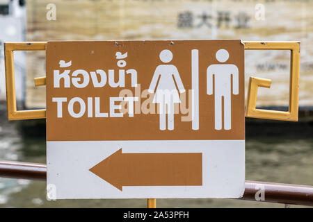 Città di Bangkok, Tailandia - 17 Marzo 2019: Direzione alla toilette più vicina strada segno è una combinazione di bianco e marrone chiaro con testo in inglese e tailandese. Foto Stock