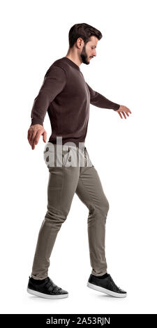 Montare un uomo in abiti casual guarda giù come egli solleva il piede durante il funambolico passi a piedi su uno sfondo bianco. Foto Stock