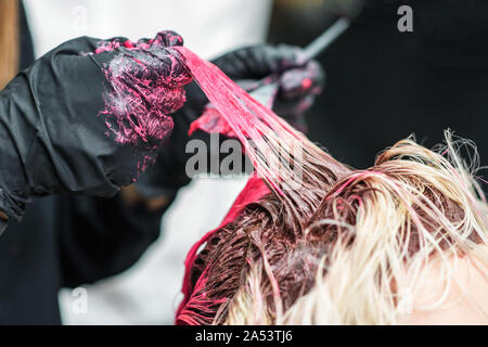 Primo piano delle mani di un parrucchiere in guanti nero dye la ciocca di capelli del client della ragazza di colore rosso. La colorazione dei capelli processo. Bellezza e moda concetto. Foto Stock