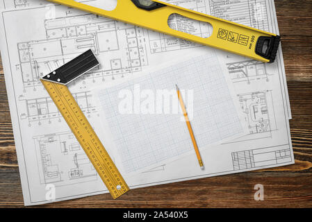 Tavolo in legno con blueprint, un righello con angolo bar, un livello di costruttori, una matita e sezione trasversale carta giacente su di esso. Foto Stock