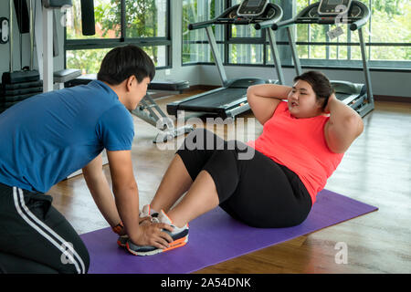 Due Asian trainer uomo e donna sovrappeso esercizio di sedersi insieme in una palestra moderna, felice e sorridere durante gli allenamenti. Grasso donne prendersi cura della salute e Foto Stock