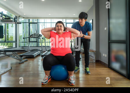 Due Asian trainer uomo e donna sovrappeso esercizio con sfera insieme in una palestra moderna, felice e sorridere durante gli allenamenti. Grasso donne prendersi cura della salute Foto Stock