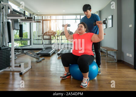 Due Asian trainer uomo e donna sovrappeso che esercitano con il manubrio e la sfera insieme in una palestra moderna, felice e sorridere durante gli allenamenti. Donne Grasse prendete ca Foto Stock