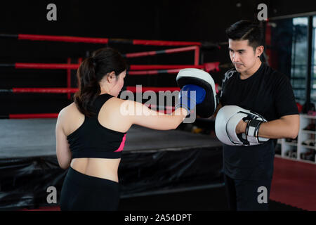 Giovane donna asiatica boxer colpisce con punzone dritto al trainer professionale nella boxe studuim in background in palestra per il fitness. Montare sportivo per un sano Foto Stock