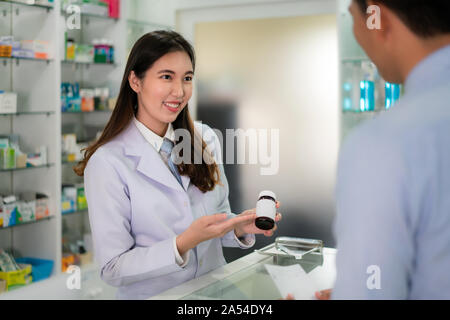 Fiducioso asiatici femmina giovane farmacista con un bel sorriso amichevole e spiegando la medicina per il suo cliente in farmacia farmacia. Medicina, PHA Foto Stock