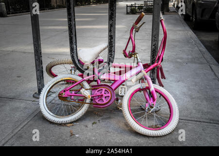 Due vecchi la ragazza di biciclette, arrugginiti e a lungo dimenticato, incatenato ad un portabiciclette, su New York City street Foto Stock