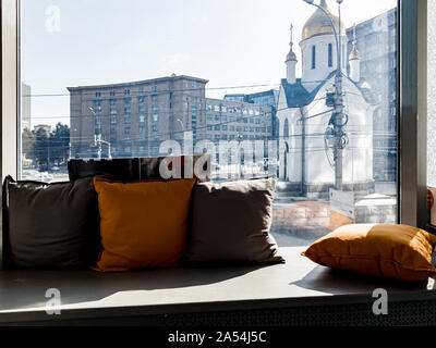 Una finestra con un davanzale sul quale giacciono i cuscini con una vista della città e l'attrazione di una piccola cappella con una cupola dorata a Novosibirsk. Foto Stock