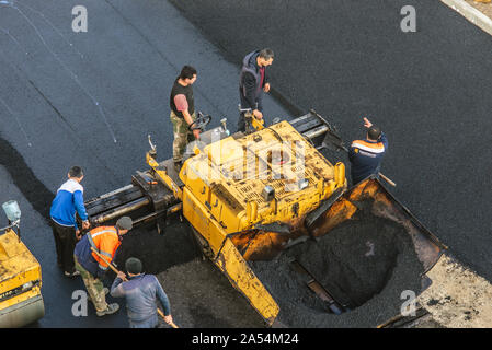 Lavoratori deporre un nuovo rivestimento in asfalto utilizzando bitume caldo. Lavoro di macchinari pesanti e lastricatore. La vista dall'alto Foto Stock